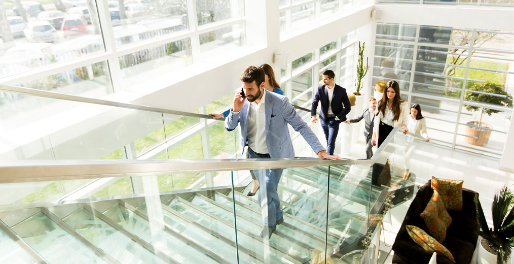 Geschäftsleute auf der Treppe im Bürogebäude Mehrere Personen in Businesskleidung gehen eine gläserne Treppe in einem hellen, modernen Bürogebäude hinauf.