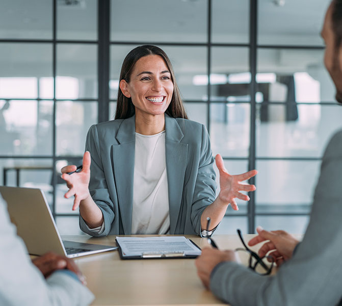 Eine Frau spricht lächelnd mit zwei Kollegen in einem modernen Besprechungsraum.