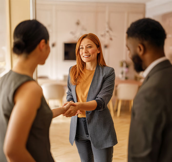 Begrüßung beim Bewerbungsgespräch Drei Personen stehen in einem freundlich eingerichteten Raum, während eine Frau einer Bewerberin die Hand schüttelt – Symbol für ein erfolgreiches Bewerbungsgespräch.