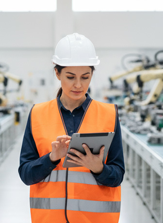 Ihr Weg zu Projekten und Positionen Ingenieurin mit Schutzhelm und Sicherheitsweste arbeitet mit Tablet in einer modernen Produktionshalle.