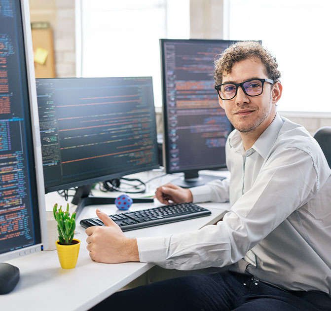 IT-Spezialist am Arbeitsplatz Ein Programmierer sitzt am Schreibtisch vor zwei Monitoren mit Code und arbeitet konzentriert.