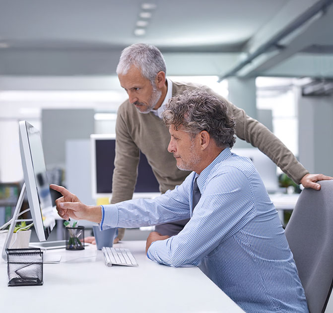 IT-Experten analysieren Daten am Computer Zwei Männer arbeiten gemeinsam an einem Bildschirm und besprechen technische Details in einem hellen Büro.