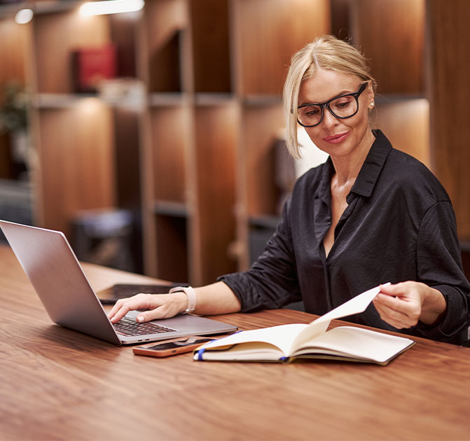 Juristin bei der Aktenprüfung Eine Frau mit Brille sitzt an einem Schreibtisch, arbeitet am Laptop und prüft gleichzeitig Unterlagen – Symbol für den Rechts- und Compliance-Bereich.