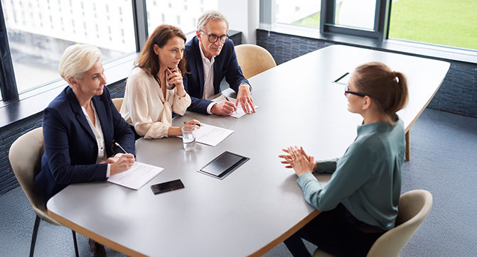 Drei Recruiter führen ein Gespräch mit einer Bewerberin in einem hellen Meetingraum.