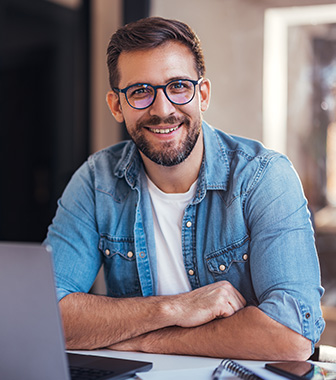 Geschäftsmann mit Brille arbeitet lächelnd am Laptop in modernem Büro.