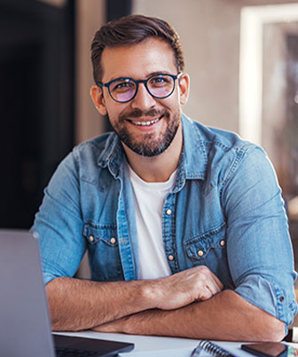 Geschäftsmann mit Brille arbeitet lächelnd am Laptop in modernem Büro.