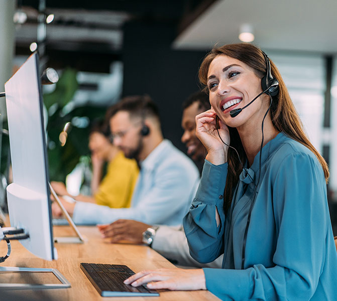 Mitarbeiterin im Callcenter Eine lächelnde Frau mit Headset arbeitet an einem Computer in einem modernen Büro.