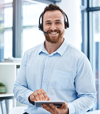 Mehr als Unterstützung: Callcenter Agent in Bielefeld Freundlicher Callcenter-Mitarbeiter mit Headset und Tablet lächelt im Büro.