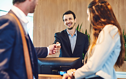 Empfangsmitarbeiter in Bielefeld Mitarbeiter am Empfang begrüßt freundlich Gäste und übergibt eine Schlüsselkarte.