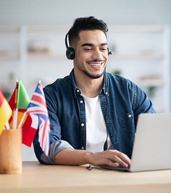 Mehr als Unterstützung: Fremdsprachenkorrespondent in Frankfurt Mann mit Headset und internationalen Flaggen arbeitet am Laptop – Experte für Sprachen und Übersetzungen.