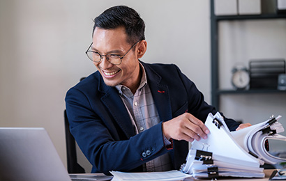 Rechtsanwaltsfachangestellter in Bielefeld Geschäftsmann mit Brille sortiert Unterlagen am Schreibtisch und lacht.