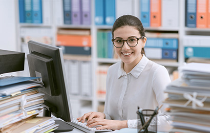 Sachbearbeiter in Bielefeld Junge Frau arbeitet am PC im Büro und lächelt in die Kamera.