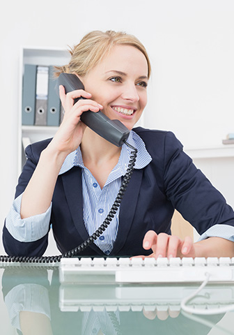 Frau am Telefon im Büro Eine Frau sitzt an ihrem Arbeitsplatz, telefoniert lächelnd und tippt gleichzeitig auf ihrer Tastatur.