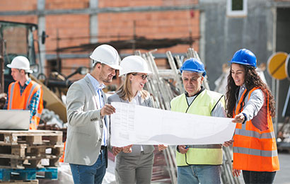 Team auf Baustelle mit Bauplänen Vier Personen mit Schutzhelmen betrachten gemeinsam Baupläne auf einer Baustelle.