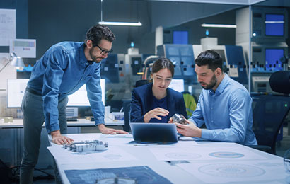 Ingenieurteam bei der Produktentwicklung Drei Personen besprechen technische Zeichnungen und Bauteile an einem Tisch im Büro.