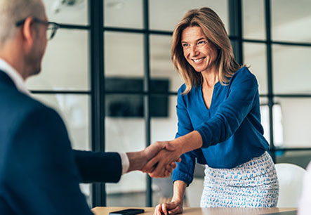 Frau begrüßt Geschäftspartner mit Handschlag im Büro Lächelnde Frau in blauer Bluse schüttelt einem Kollegen im Besprechungsraum die Hand.