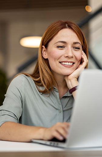 Engagierte Mitarbeiterin am Laptop Junge Frau arbeitet motiviert am Laptop und lächelt während eines Videocalls im Büro.