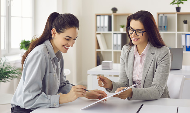 Vertragsunterschift zwischen 2 Frauen an einem Schreibtisch Vertragsunterschift zwischen 2 Frauen an einem Schreibtisch