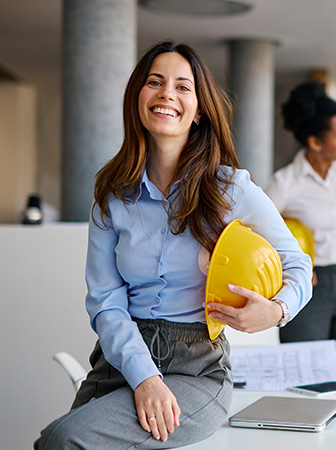Lächelnde Frau mit Helm an einem Schreibtisch