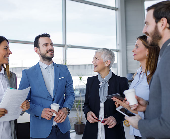 Teamgespräch in moderner Büroumgebung Vier Kolleginnen und Kollegen unterhalten sich in einem hellen Bürogebäude und lächeln – Symbol für erfolgreiche Zusammenarbeit und Kommunikation im Team.