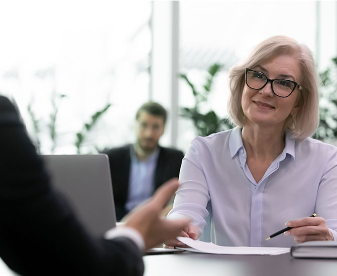 Eine Frau mit Brille führt ein professionelles Gespräch an einem Schreibtisch in einem modernen Büro.