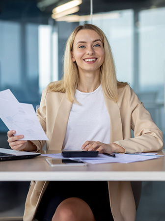 Frau sitzt am Schreibtisch, hält Dokumente in der Hand und lächelt freundlich.