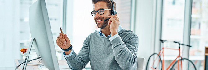 Lächelnder Mann spricht mit Headset am Computer in einem modernen Büro.