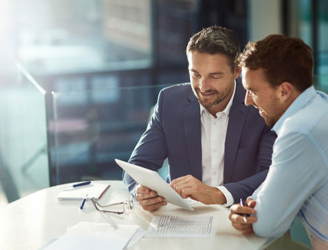 Zwei Gesch&auml;ftsm&auml;nner sehen gemeinsam auf ein Tablet und besprechen Recruiting-Strategien.