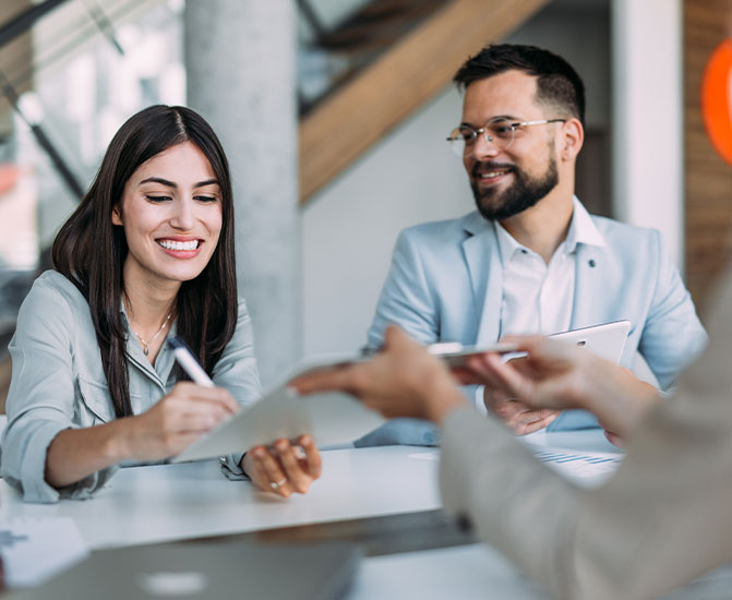 Vertrag wird unterschrieben Zwei Personen sitzen an einem Tisch, lächeln und unterzeichnen gemeinsam ein Dokument.