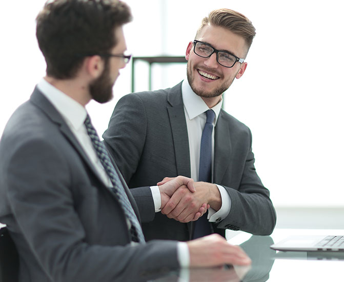Handschlag zwischen Geschäftspartnern Zwei Männer im Anzug sitzen an einem Tisch und begrüßen sich mit einem freundlichen Händedruck.