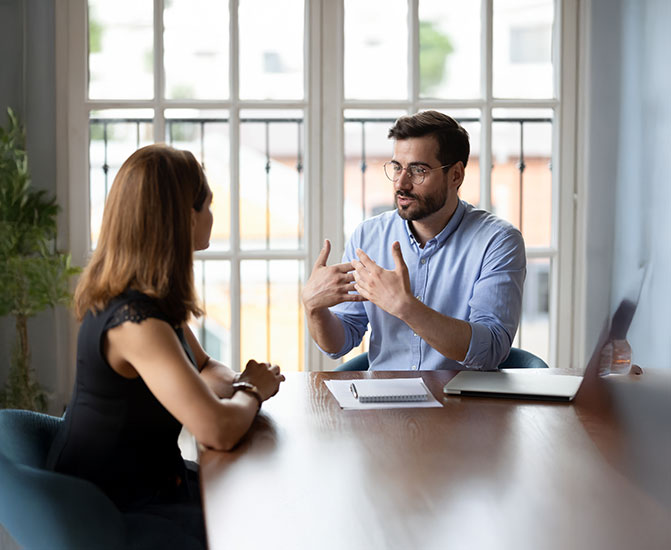Ein Mann und eine Frau sitzen sich an einem Tisch gegenüber und führen ein konzentriertes Gespräch.
