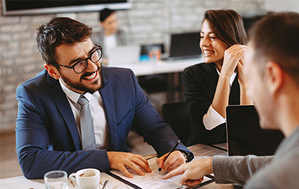 Präzise und unkompliziert Geschäftsmann bespricht Unterlagen mit Kollegen und lächelt während des Gesprächs.