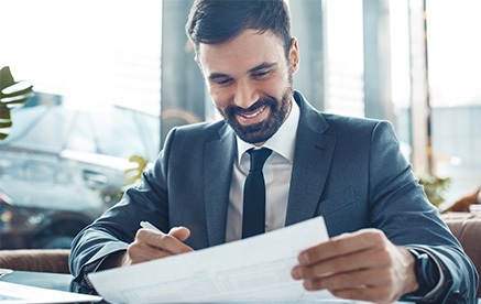 Skalierbar und strategisch Geschäftsmann im Anzug prüft Dokumente und lächelt zufrieden.