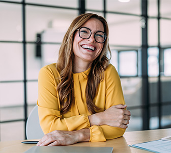 Lachende Frau mit Brille im Büro Freundlich lächelnde Frau mit Brille und gelber Bluse sitzt in modernem Büro.